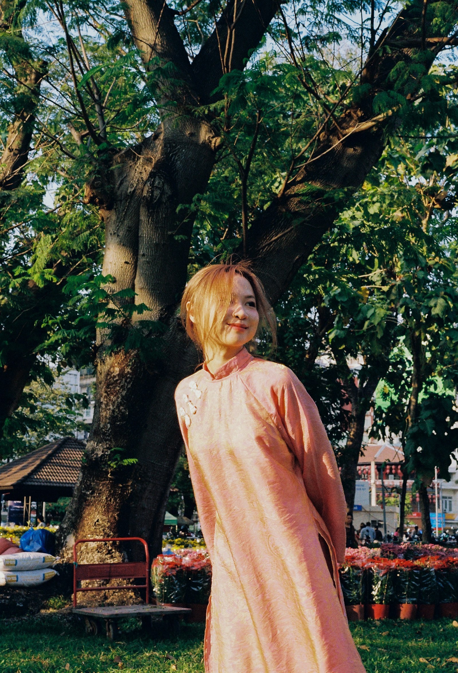 Woman in a pink dress standing in a park framed by soft greenery.