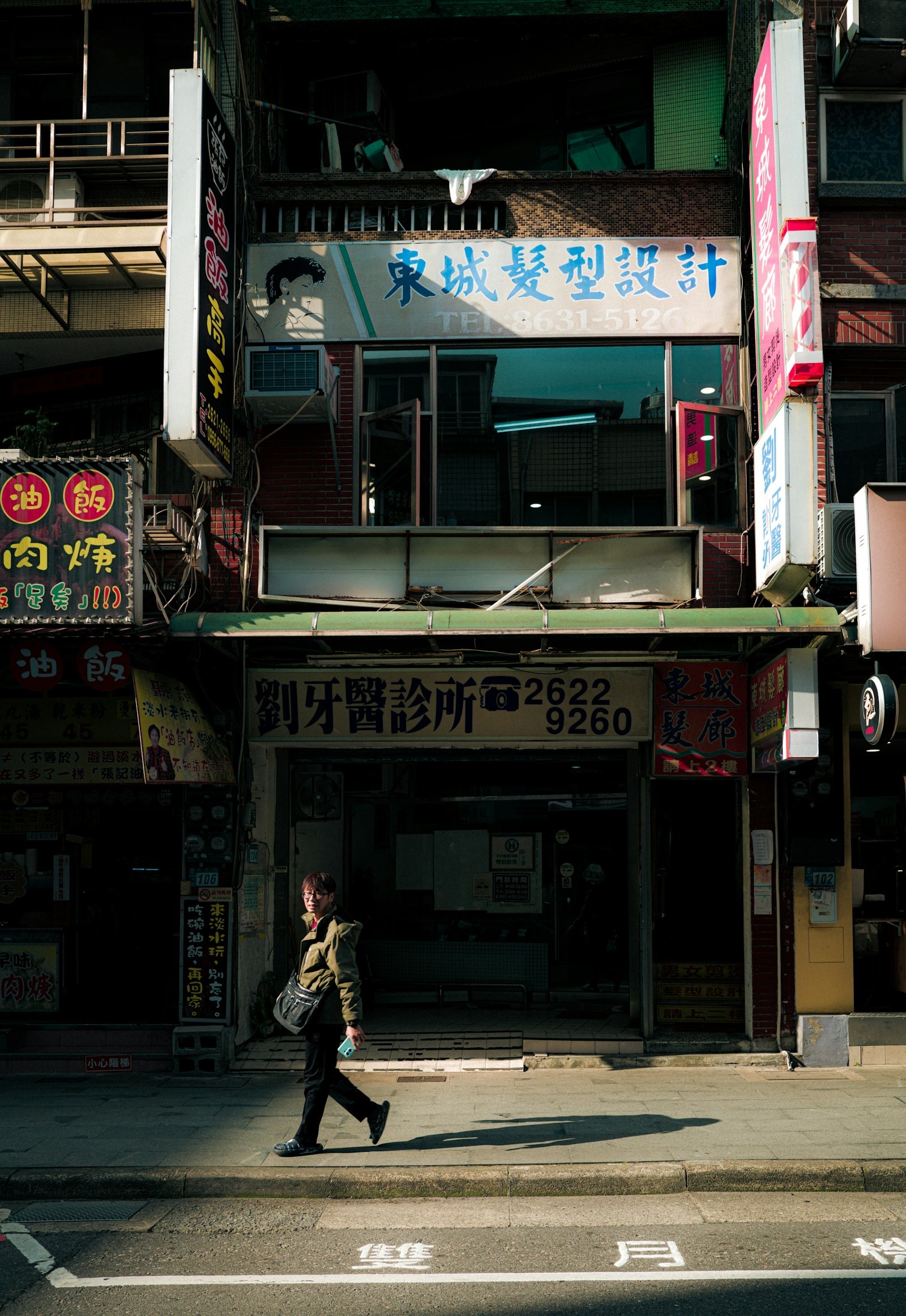 Woman walking past shopfronts on a bright sunny street.